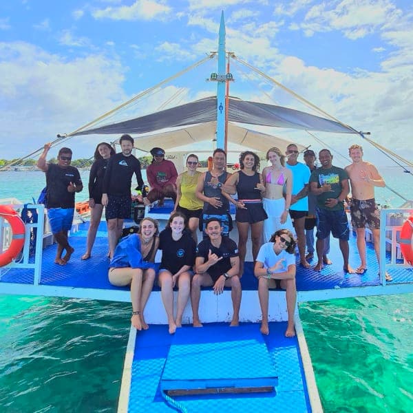 Divers gathered on the deck of an MBI bangka dive boat over turquoise water, Malapascua